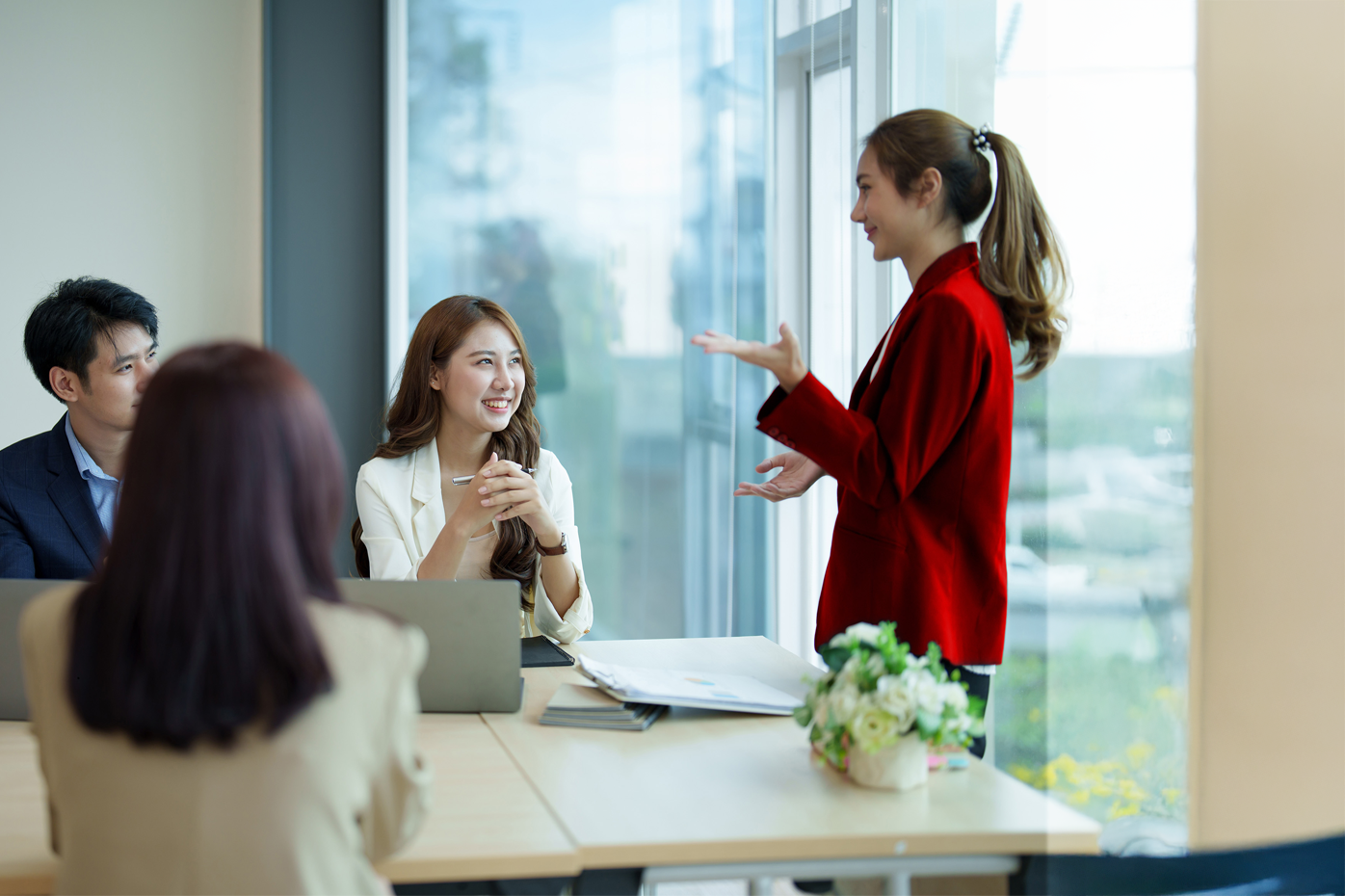 A woman in a red blazer speaks to a group of people
